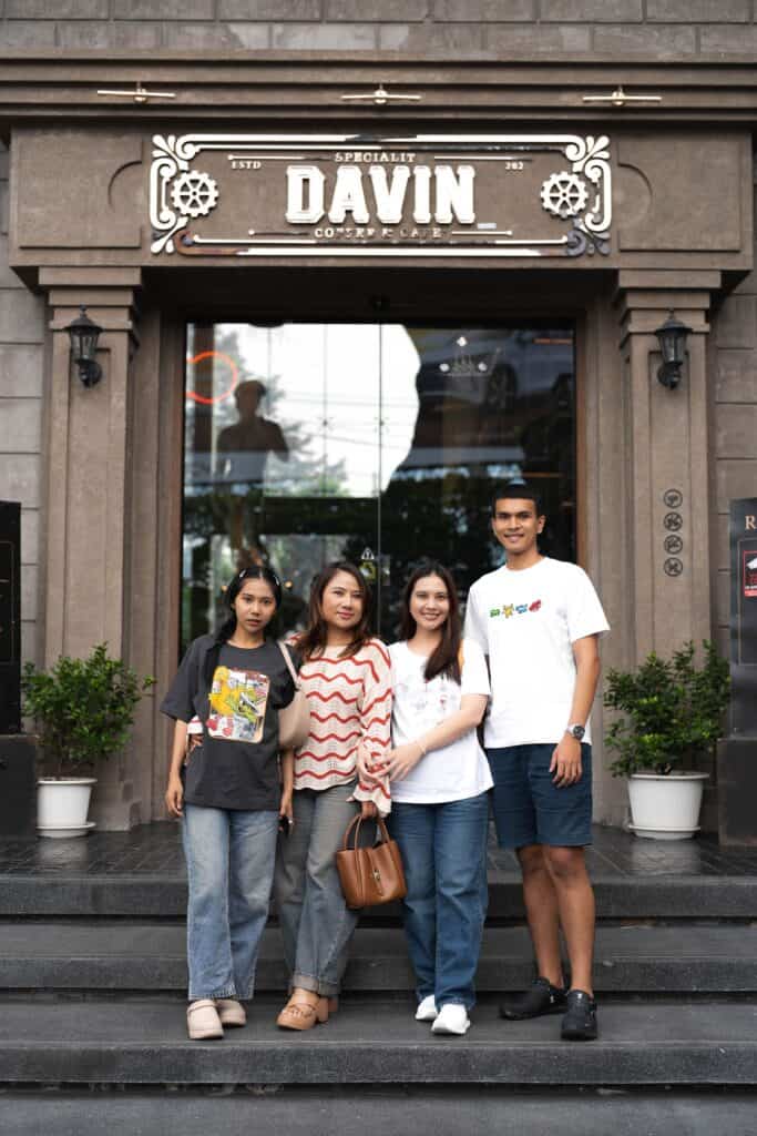 A group of four friends posing for a photo on the steps outside the main entrance of Davin Cafe.