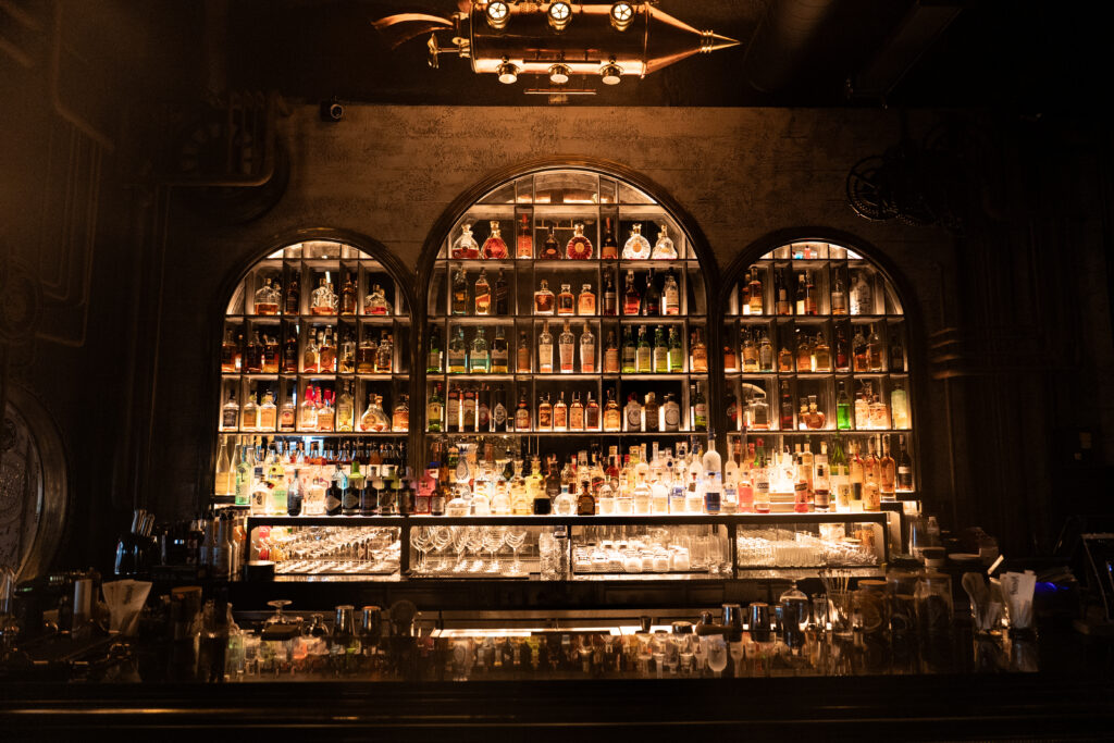 Backlit premium liquor display inside a luxury cocktail bar in Bangkok, featuring curated spirits and an intimate speakeasy atmosphere for elevated dining and nightlife experiences