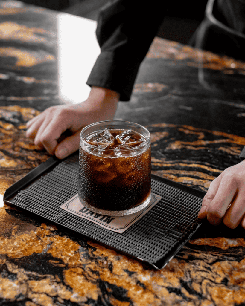 Cold Brew ซิกเนเจอร์จาก DAVIN CAFE เสิร์ฟพร้อมน้ำแข็งในแก้วเย็น แสดงเอกลักษณ์ของกาแฟสกัดเย็นที่ให้รสชาตินุ่มลึก หวานธรรมชาติ และกลิ่นหอมชัดเจน เหมาะสำหรับผู้ที่มองหาประสบการณ์ Specialty Cold Brew ระดับพรีเมียม