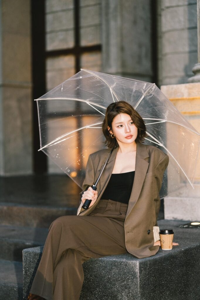 Cafe photo poses with a seated fashion look holding a clear umbrella beside coffee and Roman-inspired architecture at DAVIN CAFE Ramintra